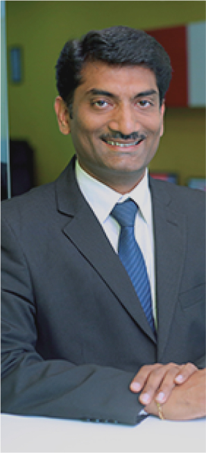 Man in a formal suit smiling, standing indoors.