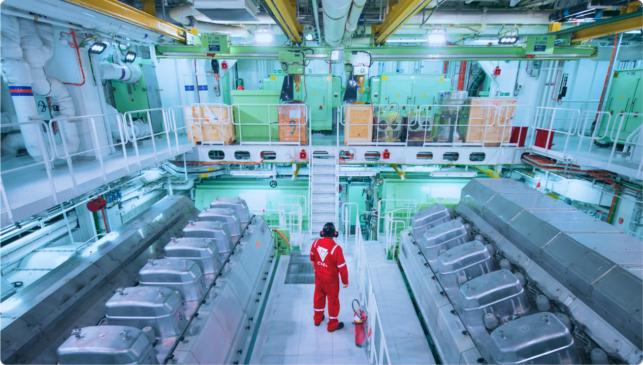 Engineer in red safety suit inspecting large ship engine room with industrial machinery on both sides.